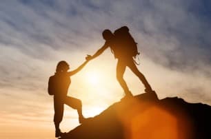 Two hikers helping each other reach the summit